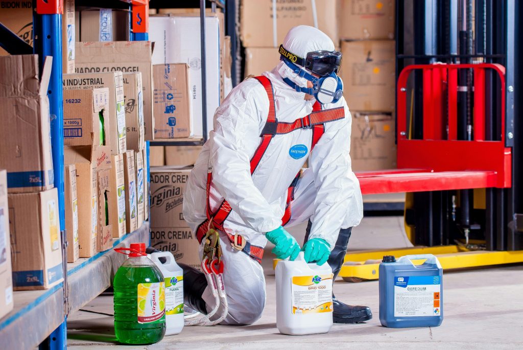 A man cleaning a warehouse using toxic chemicals, wearing a protective suit and breather.