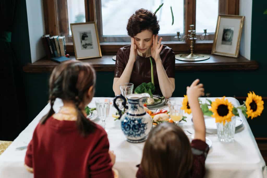 A grandma holding her head frustrated as her two grandchildren ask her questions.