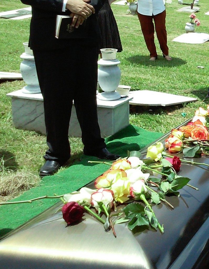 A pastor finishes reading from a Bible as a coffin is lowered into a grave.