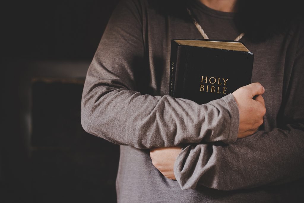 Hands folded in prayer on a Holy Bible in church. Image by jcomp on Magnific