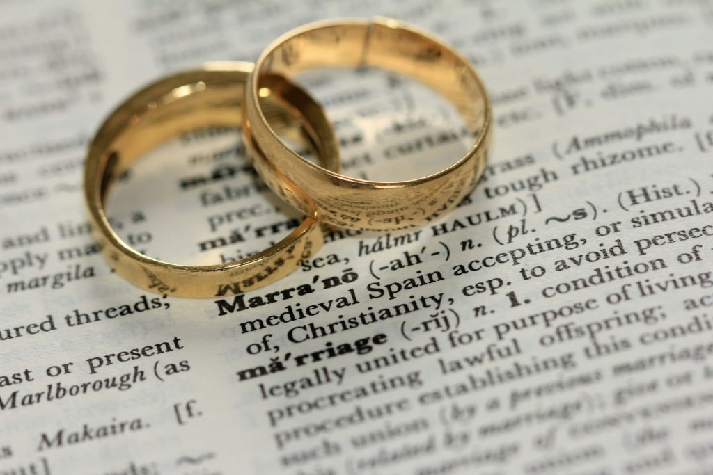 Two wedding bands laying together on top of a dictionary turned to the definition of marriage