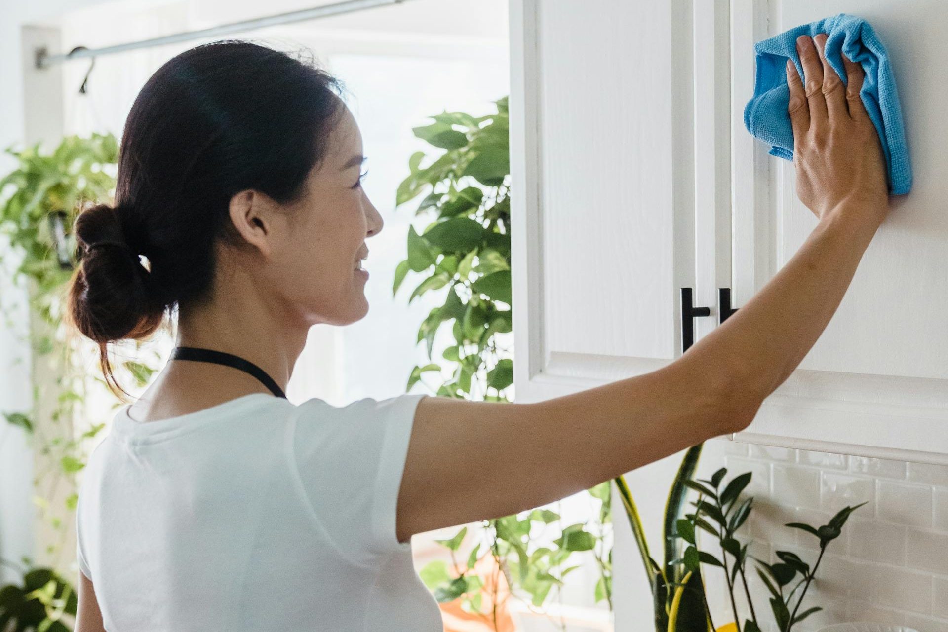 A woman uses her practical tips to keep her house clean wiping down the cabinets.